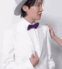 a man wearing a white suit and a purple bow tie is being touched by a woman .
