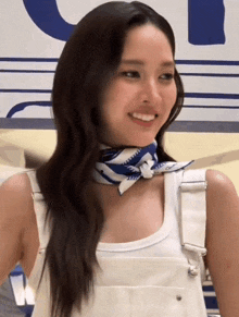 a woman wearing overalls and a scarf around her neck smiles for the camera