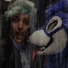 a man with green hair is standing next to a blue and white stuffed animal