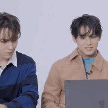 two young men are sitting next to each other and one is using an apple laptop