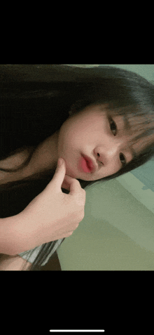 a girl with long black hair is taking a selfie with her finger on her chin