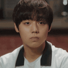 a close up of a young man 's face with a white shirt and black collar