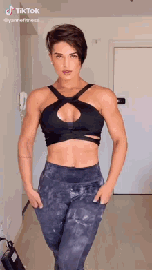 a woman with short hair is wearing a black crop top and gray leggings .