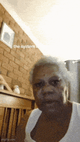 a woman in a white tank top is sitting in front of a brick wall with the words the system written on it
