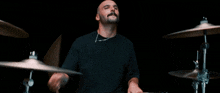 a bald man with a beard is playing a drum set in a dark room .