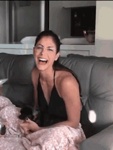 a woman wearing glasses is sitting on a couch and laughing