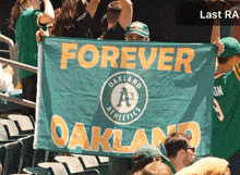 a group of people holding up a green banner that says forever oakland athletics