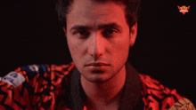 a man wearing a red shirt with a crown on it looks at the camera