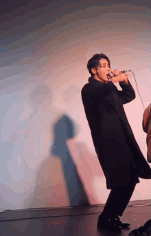 a man in a black coat is singing into a microphone on a stage