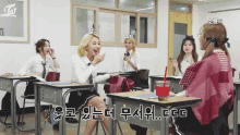 a group of girls sitting at desks in a classroom with a twice logo on the wall behind them