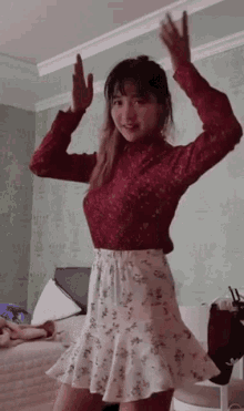 a woman in a red sweater and a white skirt is dancing in a room .