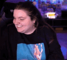 a woman is smiling while wearing a black sweater with a blue graphic on it .