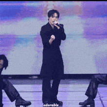 a man singing into a microphone with adorable written on the bottom right
