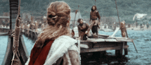 a woman in a red cape is standing on a dock in front of a body of water