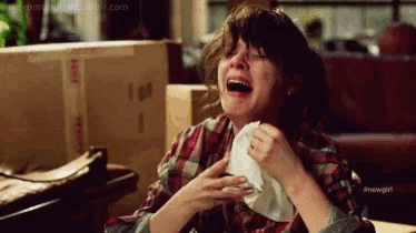 a woman is laughing and crying while holding a napkin to her face .
