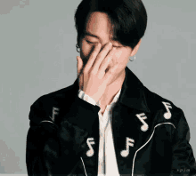 a man wearing a black jacket with music notes on it covering his mouth