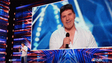 a man singing into a microphone on a stage with a nbc logo in the background