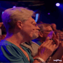 a woman in a blue shirt applauds while sitting in a dark room