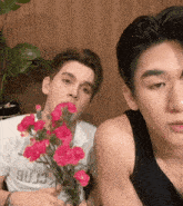 a man holding a bouquet of pink flowers next to another man wearing a tank top that says crab