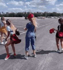 a group of women are dancing in a parking lot while holding hats .