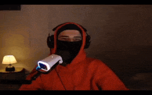 a man wearing headphones and an orange hoodie holds a microphone in his hand