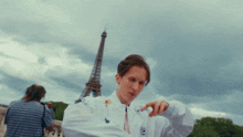 a man standing in front of the eiffel tower wearing a white jacket