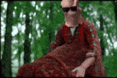 a man wearing a mask and sunglasses is sitting on a large rock .