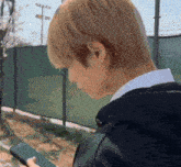 a man is looking at a cell phone in front of a fence