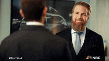 a man with a beard is smiling in front of a nbc sign
