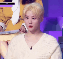 a man with blonde hair is wearing a white sweater and a microphone .