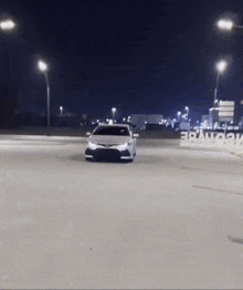 a white car is driving down a street at night with a sign in the background that says maybe
