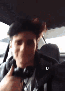 a man wearing headphones is sitting in a car with the letters ij above his head