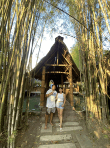 a man and a woman are standing in front of a wooden structure surrounded by bamboo