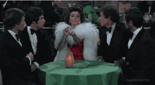 a woman in a red dress is sitting at a table with three men in suits .