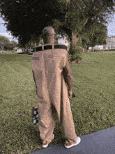 a man in overalls is standing in the grass holding a skateboard
