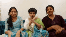 three women are sitting on a couch and one is wearing a blue dress
