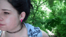 a woman wearing a choker and pink earrings is standing in the woods