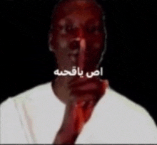 a man in a white shirt is holding his finger to his lips .