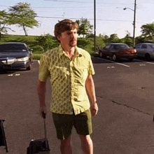 a man in a yellow shirt carrying a suitcase in a parking lot