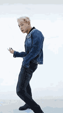 a man in a blue denim jacket and black pants is dancing .