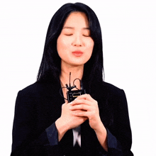 a woman in a black jacket is holding a small device with the letter e on it