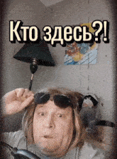 a man wearing sunglasses and a wig is holding a lamp in front of a sign that says kto zdes