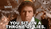 a man in a green elf costume is sitting on a throne of lies in front of a christmas tree .