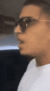 a man wearing sunglasses and a white shirt is talking .