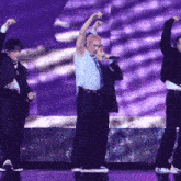 a group of men are performing on a stage with purple lights behind them
