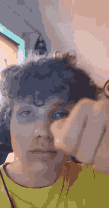 a person with curly hair is making a funny face while wearing glasses and a yellow shirt .