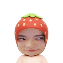 a man wearing a strawberry hat looks at the camera