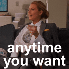 a woman in a suit sits on a couch holding a martini and the words anytime you want behind her