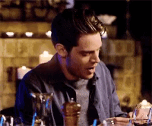 a man in a blue shirt is sitting at a table with a glass of wine in front of him .