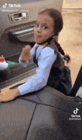 a little girl is sitting in the back seat of a car and making a funny face .